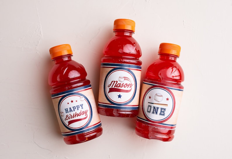 May include: Three red juice bottles with baseball-themed labels. The labels are brown with blue and red accents. One label says "Happy Birthday", one says "Mason", and one says "One".