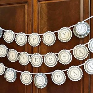 May include: A white and silver banner with the words "Happy 60th Anniversary Paul" in a circle design. The banner is hanging on a wooden door.