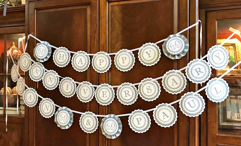 May include: A white and silver banner with the words "Happy 60th Anniversary Paul" in a circle design. The banner is hanging on a wooden door.