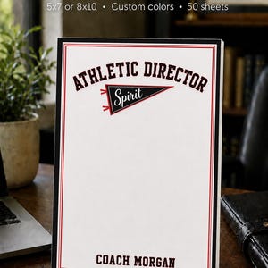 May include: A white rectangular notepad with a black and red border. The top features the text ATHLETIC DIRECTOR above a black pennant graphic with the word Spirit. The bottom displays the name COACH MORGAN in bold black capital letters.