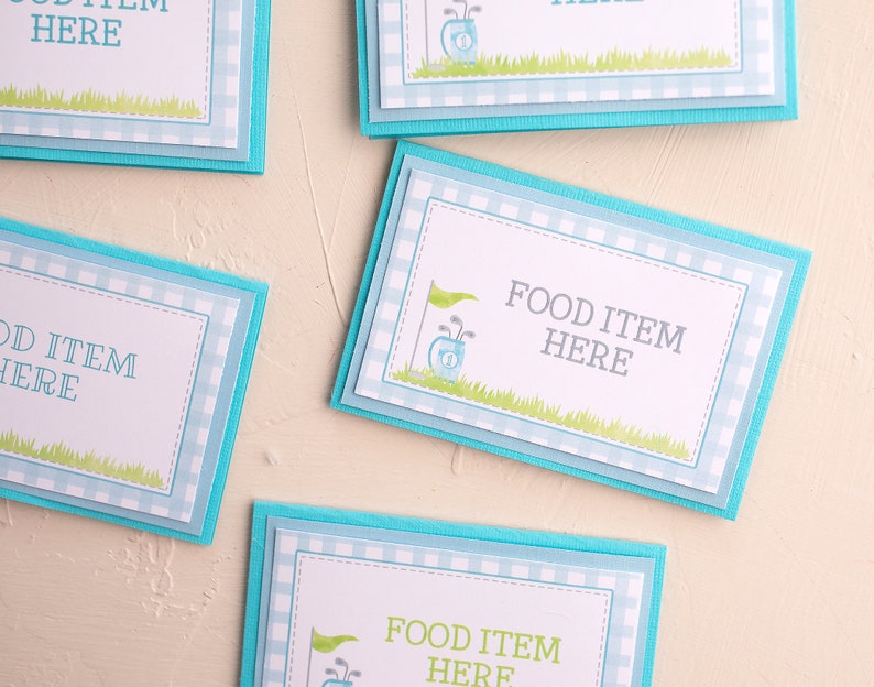 May include: Four blue and white gingham food labels with a golf bag and golf clubs graphic. The text on the labels reads "Food Item Here".