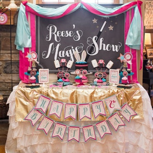 May include: A birthday party table setting with a gold tablecloth and a banner that reads "Happy 8th Birthday". The table is decorated with a magic show theme, including a chalkboard sign that says "Reese's Magic Show", cupcakes, and other decorations.