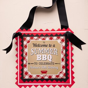 Peut inclure: Panneau d&eacute;coratif avec un ruban noir pour l'accrocher. Le panneau pr&eacute;sente un motif &agrave; carreaux rouges, noirs et blancs avec le texte "Welcome to a SUMMER BBQ to celebrate Nathan's 40th Birthday."