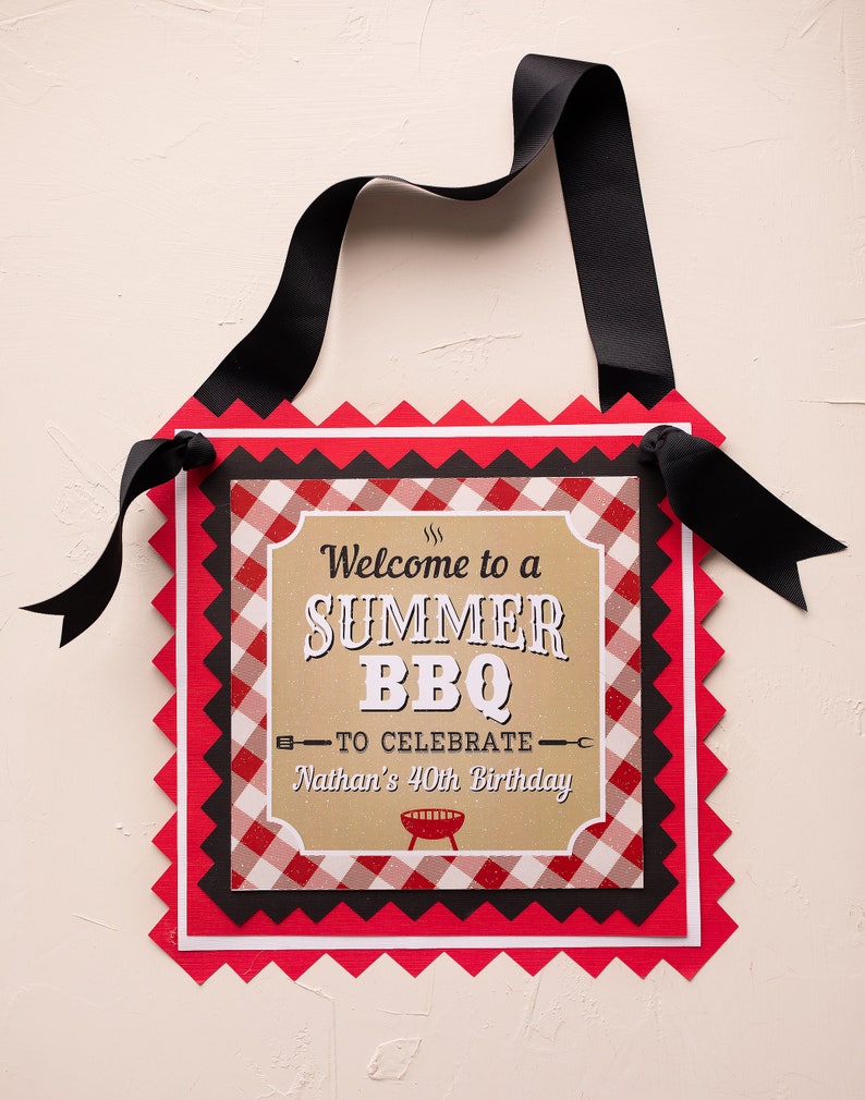 Peut inclure: Panneau d&eacute;coratif avec un ruban noir pour l'accrocher. Le panneau pr&eacute;sente un motif &agrave; carreaux rouges, noirs et blancs avec le texte "Welcome to a SUMMER BBQ to celebrate Nathan's 40th Birthday."