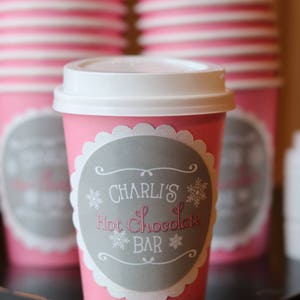 May include: Pink paper cups with white lids and a gray label that says "Charli's Hot Chocolate Bar" with snowflake designs.