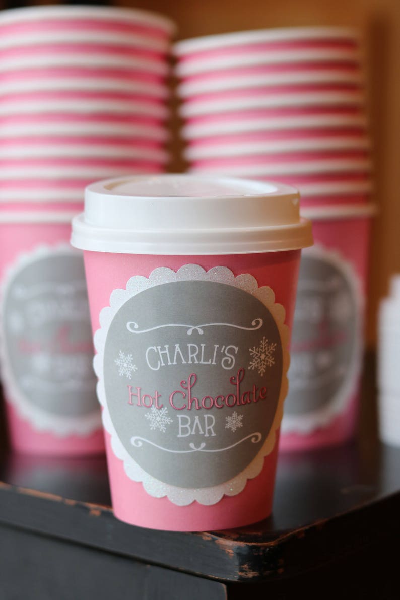 May include: Pink paper cups with white lids and a gray label that says "Charli's Hot Chocolate Bar" with snowflake designs.