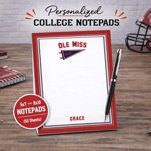 May include: A personalized college notepad with the text "OLE MISS" and a pennant logo. The notepad is red and white, with the name "GRACE" at the bottom. A pen and other Ole Miss merchandise are also visible.