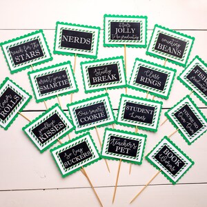 May include: A set of 15 green and black graduation party signs with white text. The signs have scalloped edges and are decorated with a white and green striped pattern. The signs feature graduation-themed puns and sayings, such as "Reach for the Stars", "Honor Rolls", "Nerds", "Aren't you a Smartie", "Study Break", "It feels Jolly to be graduating", "Counting Beans", "Class Rings", "Fishally graduating", "Goodbye Kisses", "One Smart Cookie", "So Long Suckers", "Student Loans", "You're No Dun Dun", "Teacher's Pet", and "Book Worms".