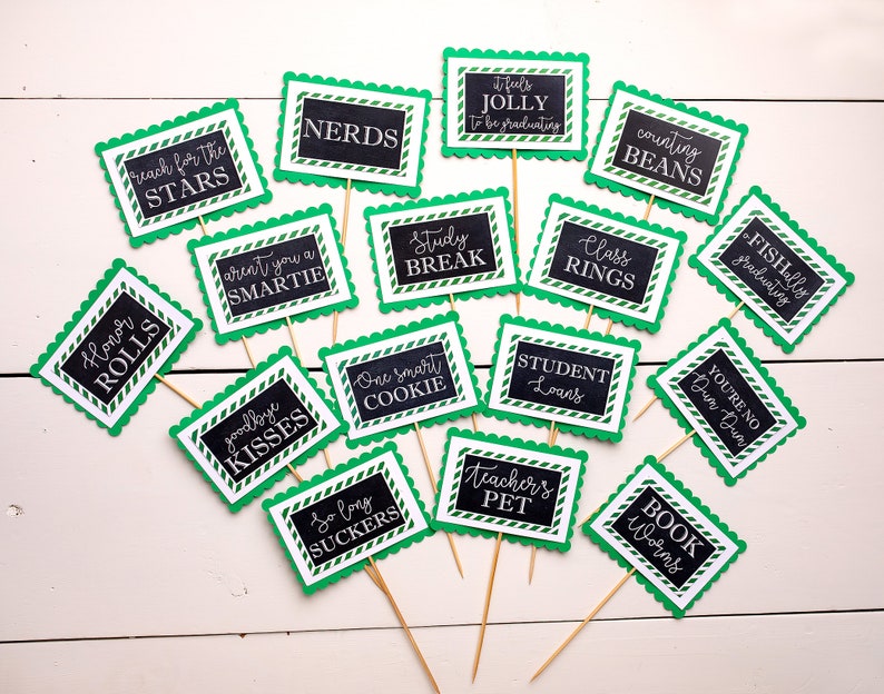 May include: A set of 15 green and black graduation party signs with white text. The signs have scalloped edges and are decorated with a white and green striped pattern. The signs feature graduation-themed puns and sayings, such as "Reach for the Stars", "Honor Rolls", "Nerds", "Aren't you a Smartie", "Study Break", "It feels Jolly to be graduating", "Counting Beans", "Class Rings", "Fishally graduating", "Goodbye Kisses", "One Smart Cookie", "So Long Suckers", "Student Loans", "You're No Dun Dun", "Teacher's Pet", and "Book Worms".