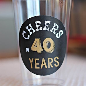May include: A clear plastic cup with a black and gold sticker that says "Cheers to 40 Years".
