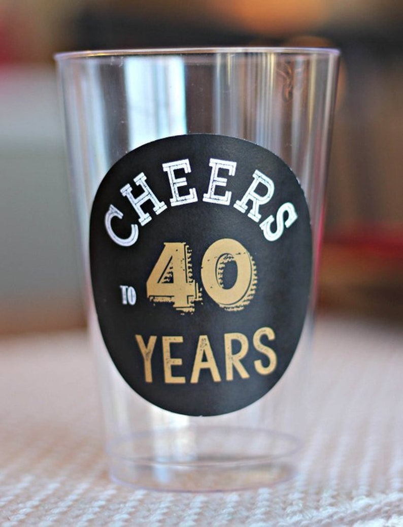 May include: A clear plastic cup with a black and gold sticker that says "Cheers to 40 Years".
