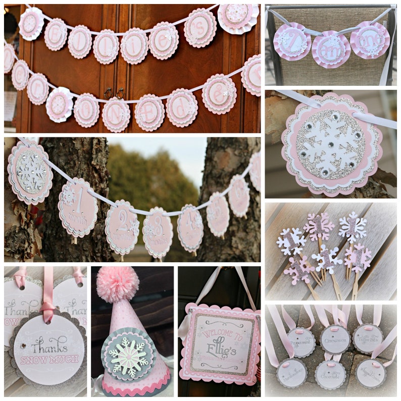 May include: A collection of pink, white, and silver party decorations featuring snowflake motifs. Items include scalloped banners spelling Ellie's One, monthly milestone markers, cupcake toppers, a party hat with a pom-pom, and signage.