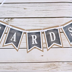 May include: A black and white banner with the word "CARDS" written on it. The banner is made of paper and has a rustic look. It is hanging from a white ribbon.