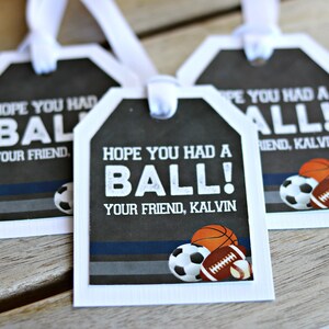 May include: Three white gift tags with black and gray backgrounds. The tags have the text "Hope you had a ball!" and "Your friend, Kalvin" printed on them. The tags are decorated with images of a soccer ball, basketball, and football.