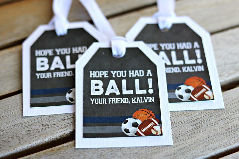 May include: Three white gift tags with black and gray backgrounds. The tags have the text "Hope you had a ball!" and "Your friend, Kalvin" printed on them. The tags are decorated with images of a soccer ball, basketball, and football.