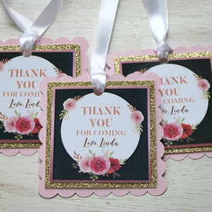 May include: Three pink and gold favor tags with a black background and floral design. The text on the tags reads "Thank You for Coming Love, Linda".