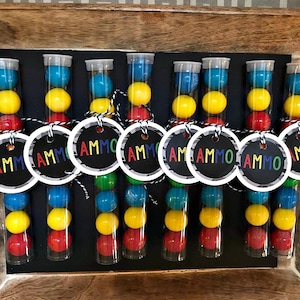 May include: Nine clear plastic tubes filled with colorful candy, each with a round tag attached that says "AMMO".