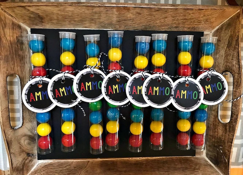 May include: Nine clear plastic tubes filled with colorful candy, each with a round tag attached that says "AMMO".