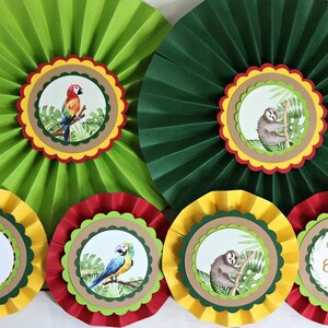 May include: Seven green, red, and yellow paper fan decorations with a jungle theme. Each fan has a different animal, including a sloth, a parrot, and a toucan. One fan has the number 7 and the words "Happy Birthday Emily".