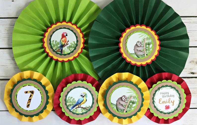 May include: Seven green, red, and yellow paper fan decorations with a jungle theme. Each fan has a different animal, including a sloth, a parrot, and a toucan. One fan has the number 7 and the words "Happy Birthday Emily".