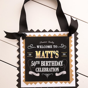 May include: Black and gold welcome sign with the text "Welcome to Matt's 50th Birthday Celebration" with a vintage design.
