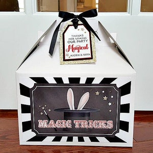 Pu&ograve; includere: Scatola regalo bianca con strisce bianche e nere. La scatola ha un'illustrazione in bianco e nero di un cappello da mago con orecchie di coniglio e il testo "Magic Tricks". Un'etichetta &egrave; attaccata alla scatola con il testo "Grazie per aver reso la nostra festa magica Kaden & Naya".