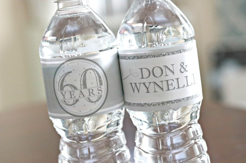May include: Two clear plastic water bottles with silver labels. One label says "60 Years" with silver glitter accents. The other label says "Don & Wynneli" with a silver swirl design.