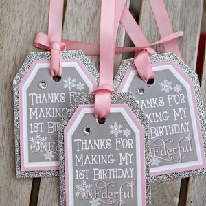 May include: Three gift tags with pink ribbons. The tags have a gray background with white text that reads "Thanks for making my 1st birthday Wonderful." The tags are outlined in silver glitter and pink.