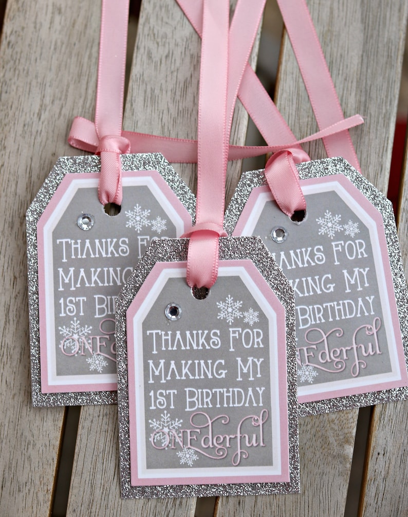 May include: Three gift tags with pink ribbons. The tags have a gray background with white text that reads "Thanks for making my 1st birthday Wonderful." The tags are outlined in silver glitter and pink.