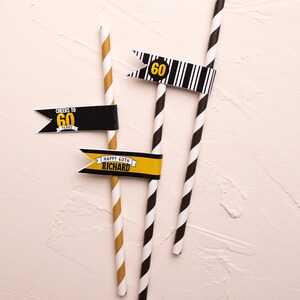 May include: Three black and white striped paper straws with flags attached. The flags are yellow and black with the text "Cheers to 60 Years", "60" and "Happy 60th Richard".