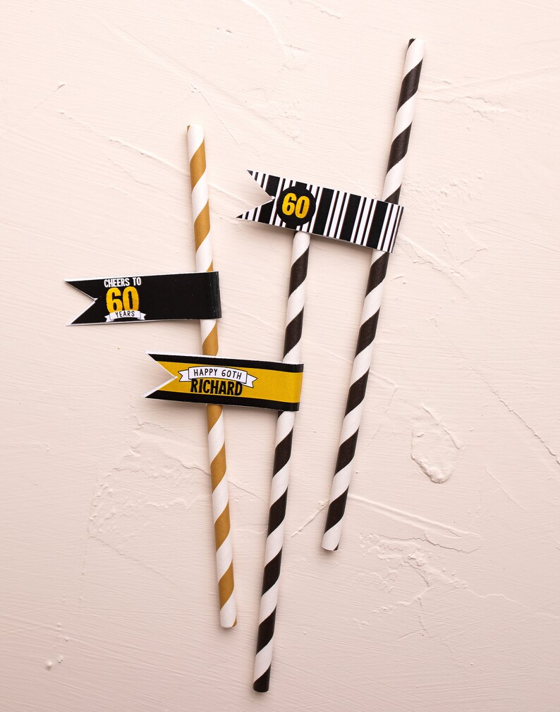 May include: Three black and white striped paper straws with flags attached. The flags are yellow and black with the text "Cheers to 60 Years", "60" and "Happy 60th Richard".