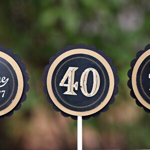 May include: Three round black and gold cupcake toppers with scalloped edges. The toppers feature the text "Vintage 1977", "40", and "Cheers to 40 Years".