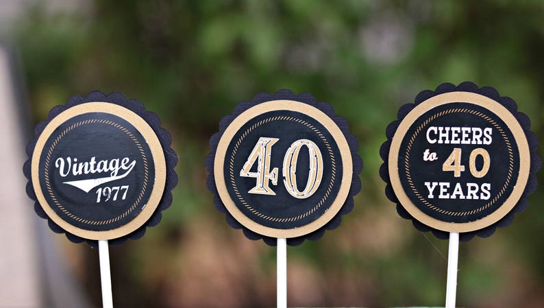 May include: Three round black and gold cupcake toppers with scalloped edges. The toppers feature the text "Vintage 1977", "40", and "Cheers to 40 Years".