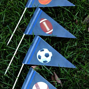 May include: Four blue pennant flags with white stripes and blue trim. Each flag features a different sport ball: basketball, football, soccer ball, and baseball.