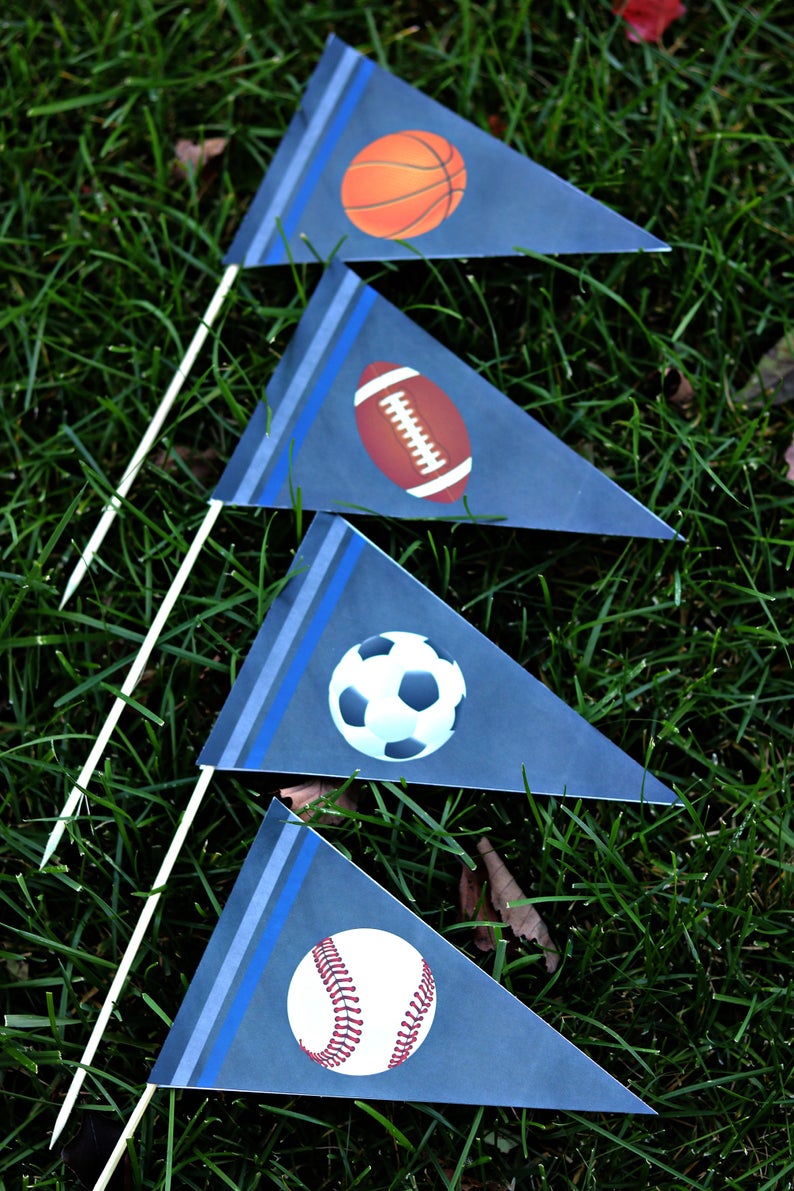 May include: Four blue pennant flags with white stripes and blue trim. Each flag features a different sport ball: basketball, football, soccer ball, and baseball.
