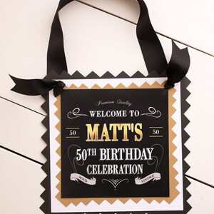 May include: Black and gold welcome sign with the text "Welcome to Matt's 50th Birthday Celebration" with a vintage design.