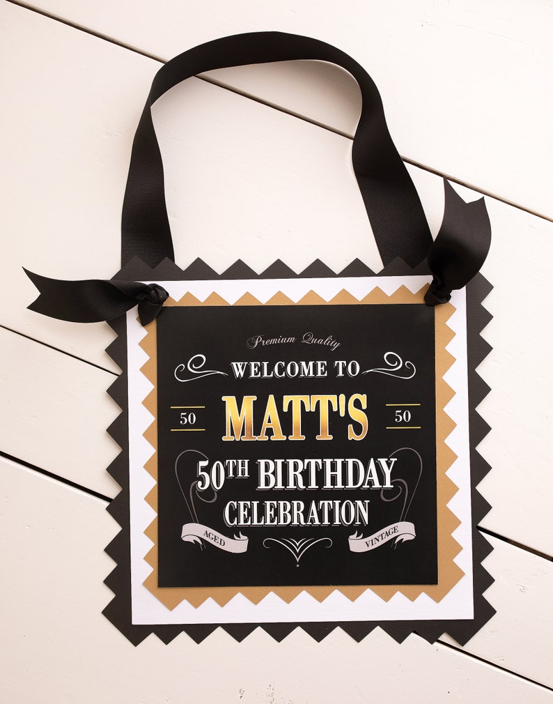 May include: Black and gold welcome sign with the text "Welcome to Matt's 50th Birthday Celebration" with a vintage design.