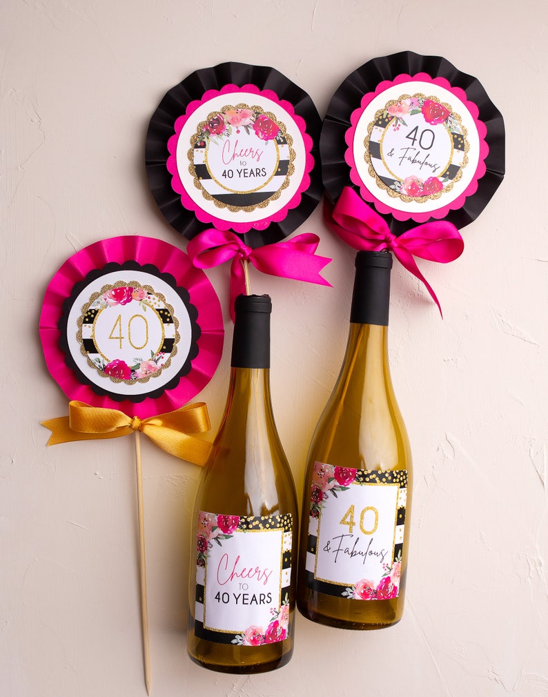 May include: Three wine bottles decorated with black and white striped labels with gold glitter and pink flowers. The labels say "Cheers to 40 Years" and "40 & Fabulous".