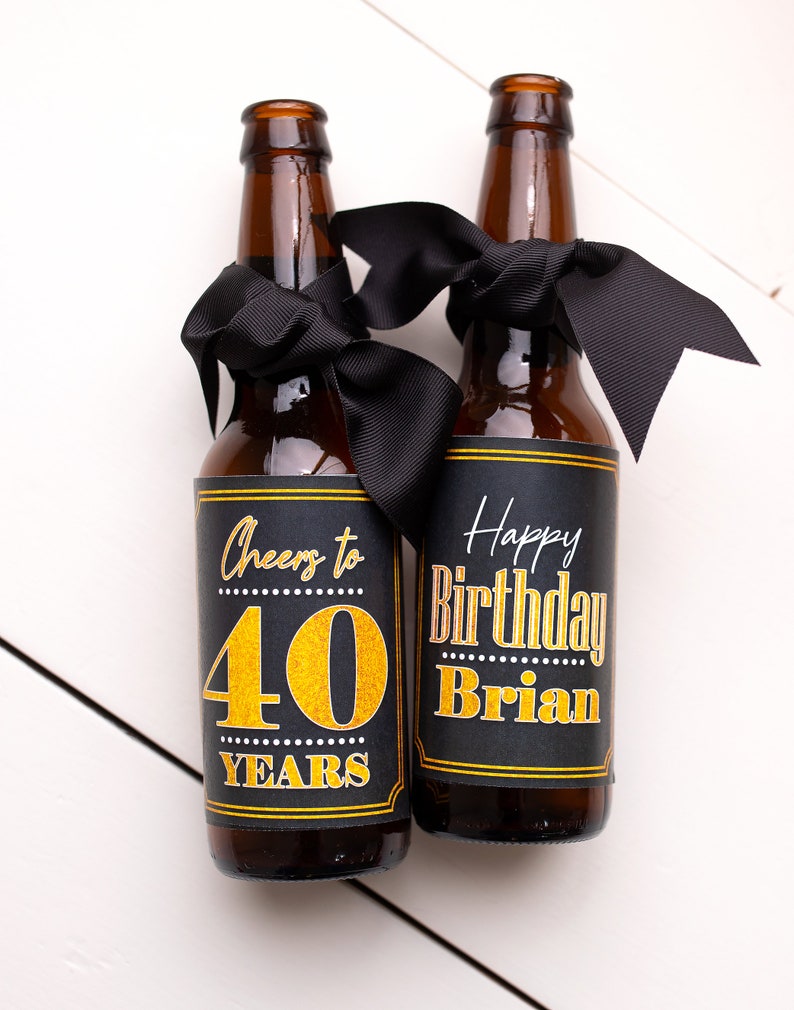 May include: Two brown glass beer bottles with black ribbon bows and personalized labels. The labels are black with gold lettering. One label says "Cheers to 40 Years" and the other says "Happy Birthday Brian".