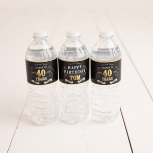 May include: Three clear plastic water bottles with black and gold labels. The labels say "Cheers to 40 Years!" and "Happy Birthday Tom".