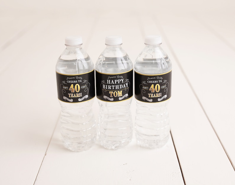 May include: Three clear plastic water bottles with black and gold labels. The labels say "Cheers to 40 Years!" and "Happy Birthday Tom".