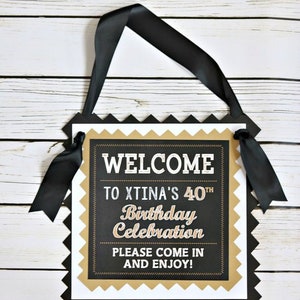 May include: Black and gold welcome sign with the text "Welcome to Xtina's 40th Birthday Celebration. Please come in and enjoy!"