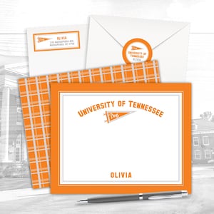 May include: Stationery set featuring the University of Tennessee logo in orange and white. Includes a card, envelope, and address labels. The card has the name "Olivia" printed on it. A pen rests on the table.