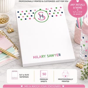 May include: A white personalized notepad featuring a green circular monogram with the initials SH, surrounded by pink, green, and navy blue polka dots. The name HILARY SAWYER is printed in pink and navy blue at the bottom. It is available in 5x7 or 8x10 inches.