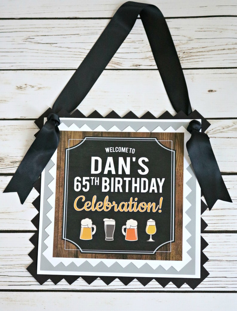 May include: Welcome to Dan's 65th Birthday Celebration! A black and white sign with a wood grain background and a chalkboard center. The sign has a scalloped border and is decorated with four beer mugs.