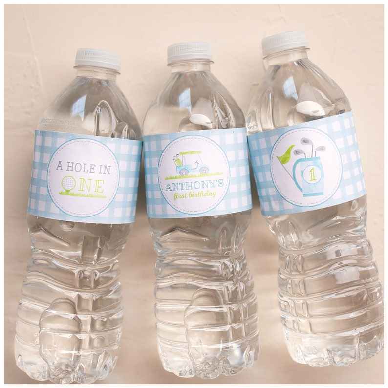 Puede incluir: Tres botellas de agua de pl&aacute;stico transparente con etiquetas a cuadros azules y blancas. Las etiquetas tienen dise&ntilde;os con tem&aacute;tica de golf y texto que dice "A Hole in One", "Anthony's First Birthday" y una bolsa de golf con palos y el n&uacute;mero "1".
