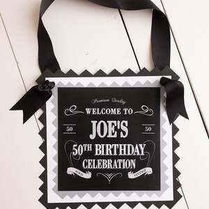 Puede incluir: Pancarta de cumplea&ntilde;os en blanco y negro con el texto "Welcome to Joe's 50th Birthday Celebration" y las palabras "Aged" y "Vintage" a cada lado del texto. La pancarta est&aacute; decorada con una cinta negra y tiene un borde festoneado.
