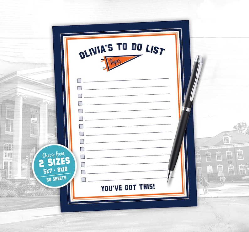 May include: A navy blue to-do list notepad with an orange and white border, and the text "OLIVIA'S TO DO LIST" at the top. A black pen rests on the notepad. The notepad includes the text "YOU'VE GOT THIS!"