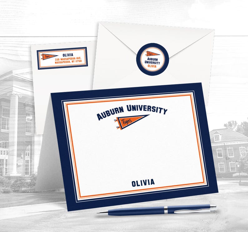May include: Auburn University branded stationery set. Includes a folded card, envelope, address label, and a round sticker. The card and label feature the name "Olivia". The set has a navy blue and orange colour scheme.