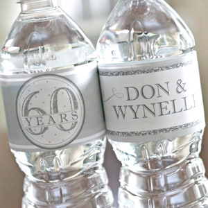 May include: Two clear plastic water bottles with silver labels. One label says "60 Years" with silver glitter accents. The other label says "Don & Wynneli" with a silver swirl design.
